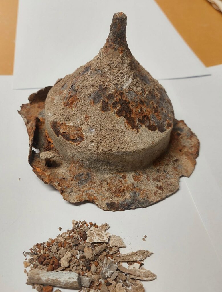Corroded second-century iron shield boss with a prominent central spike