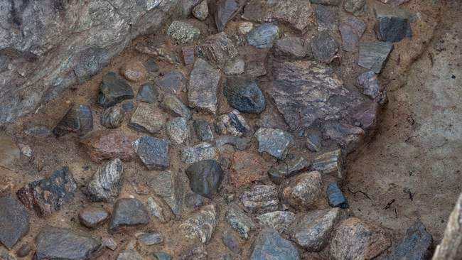Close-up of small stones of different shapes and colours set in the soil at the bottom of an excavated grave.