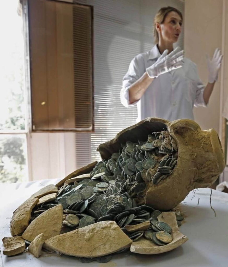 Roman bronze coins spilling from a broken amphora during conservation of the Tomares Treasure.