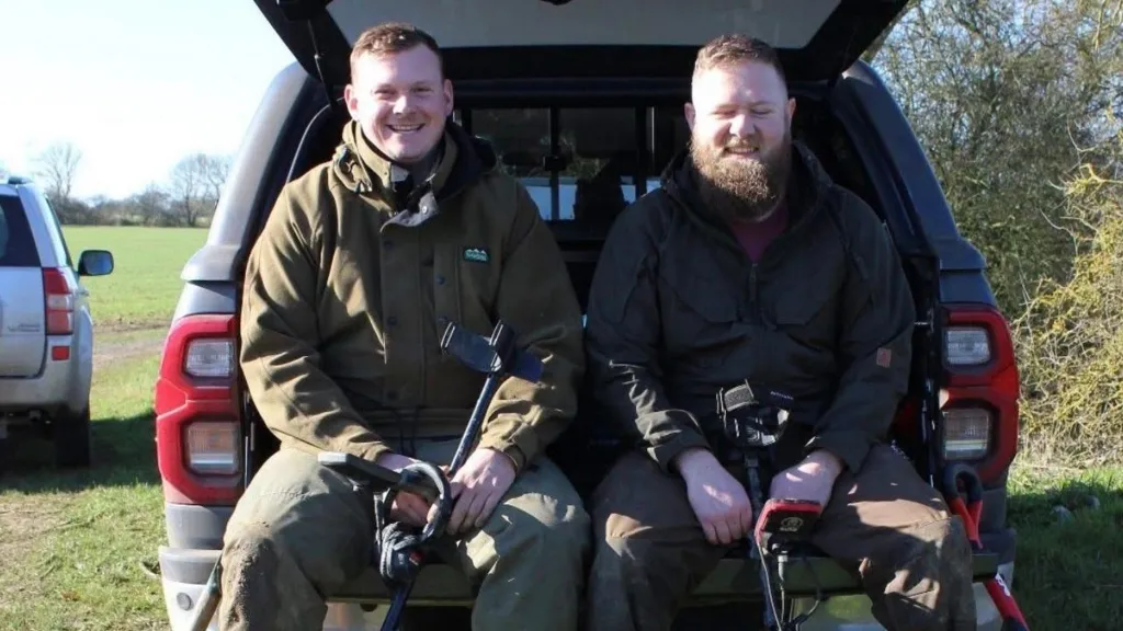 Metal detectorists Aaron Pizzey and James Race sitting beside their vehicle with metal-detecting equipment in Suffolk.