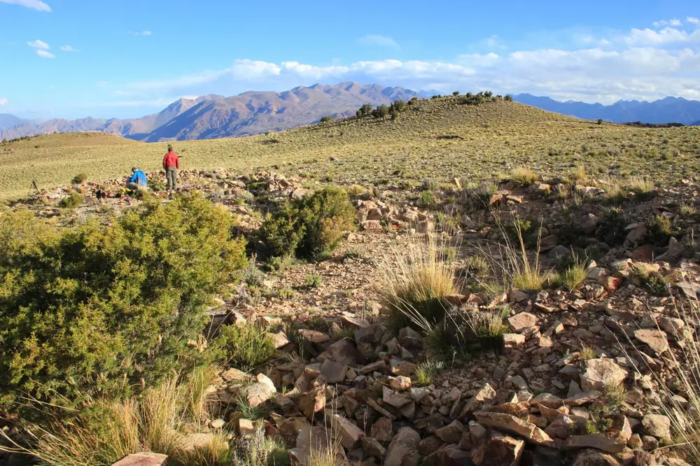 Two people standing among low stone structures in the Cordillera del Tigre.