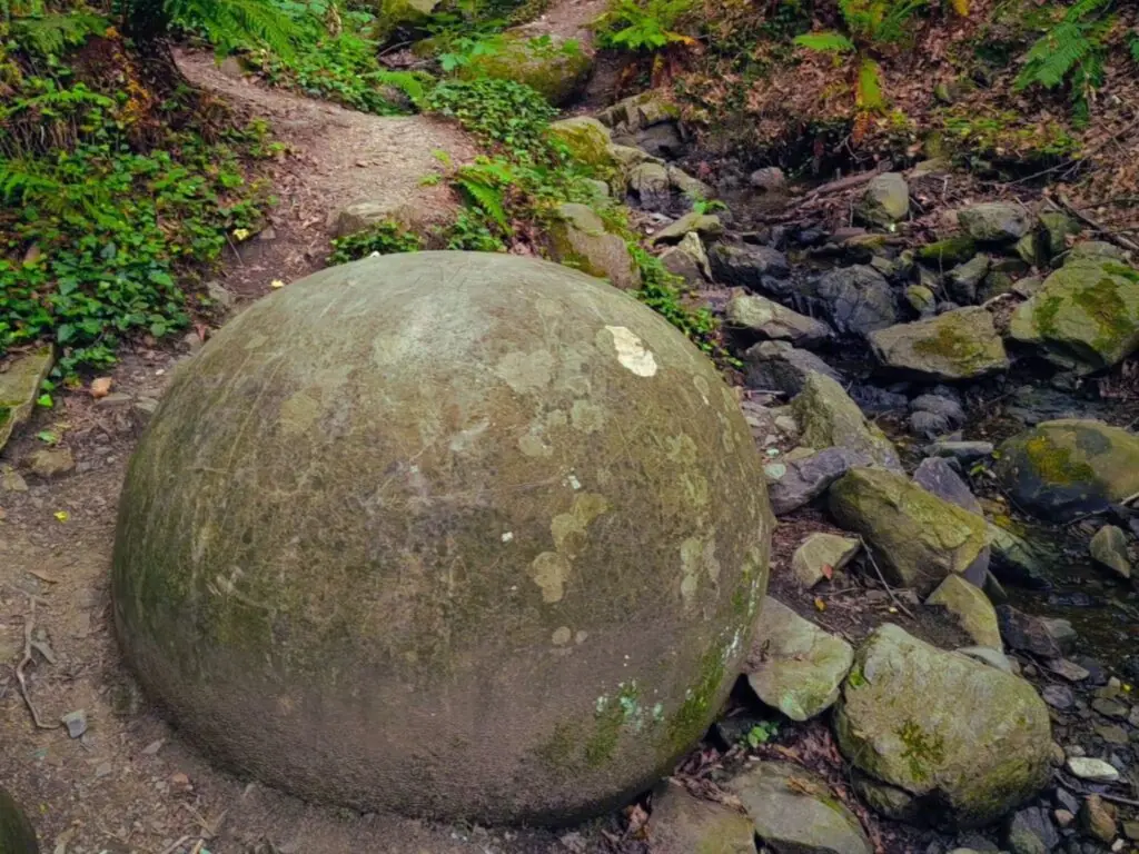 A large rounded stone sphere beside a stream near Zavidovići.