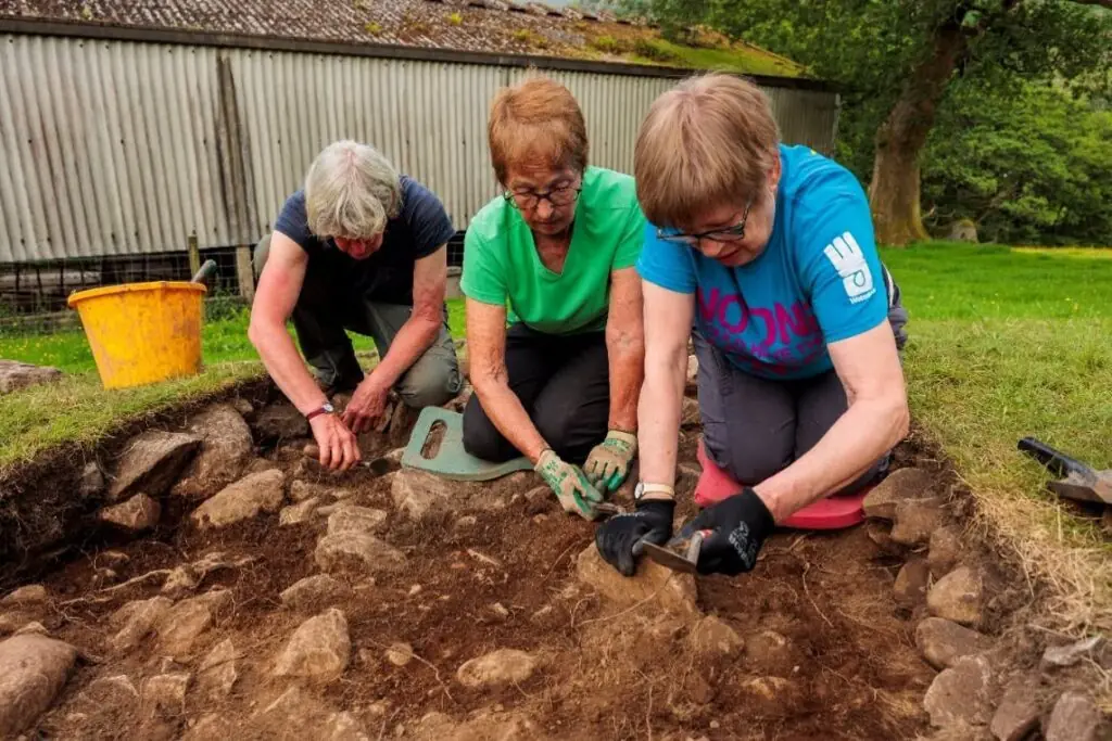 Three volunteers excavate soil and stones at Deepdale Bridge Settlement.