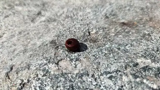 Small reddish-brown amber bead with a hole through its centre resting on a grey stone surface.