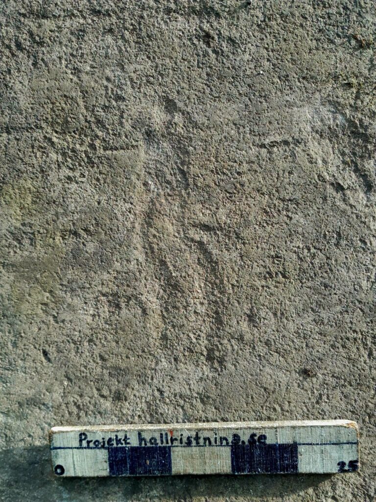 Faint human-shaped carving on granite at Trättelanda, with a measuring scale along the bottom of the image.
