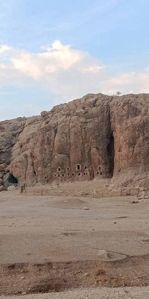 Ancient rock-cut ossuary niches scattered across a cliff face near Naqsh-e Rostam, Iran.