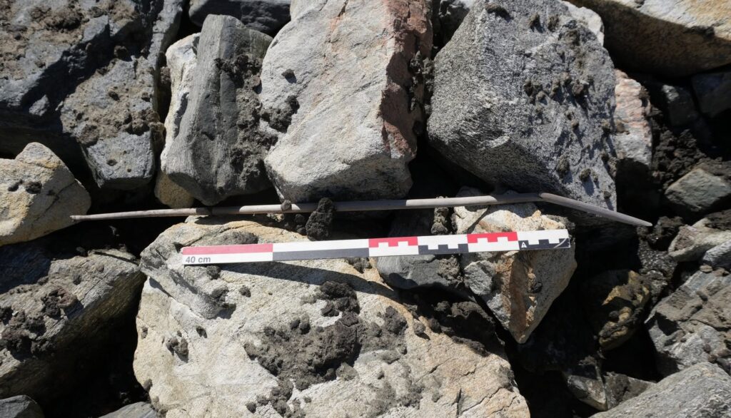 Ancient arrow lying among mountain rocks beside an archaeological measuring scale.