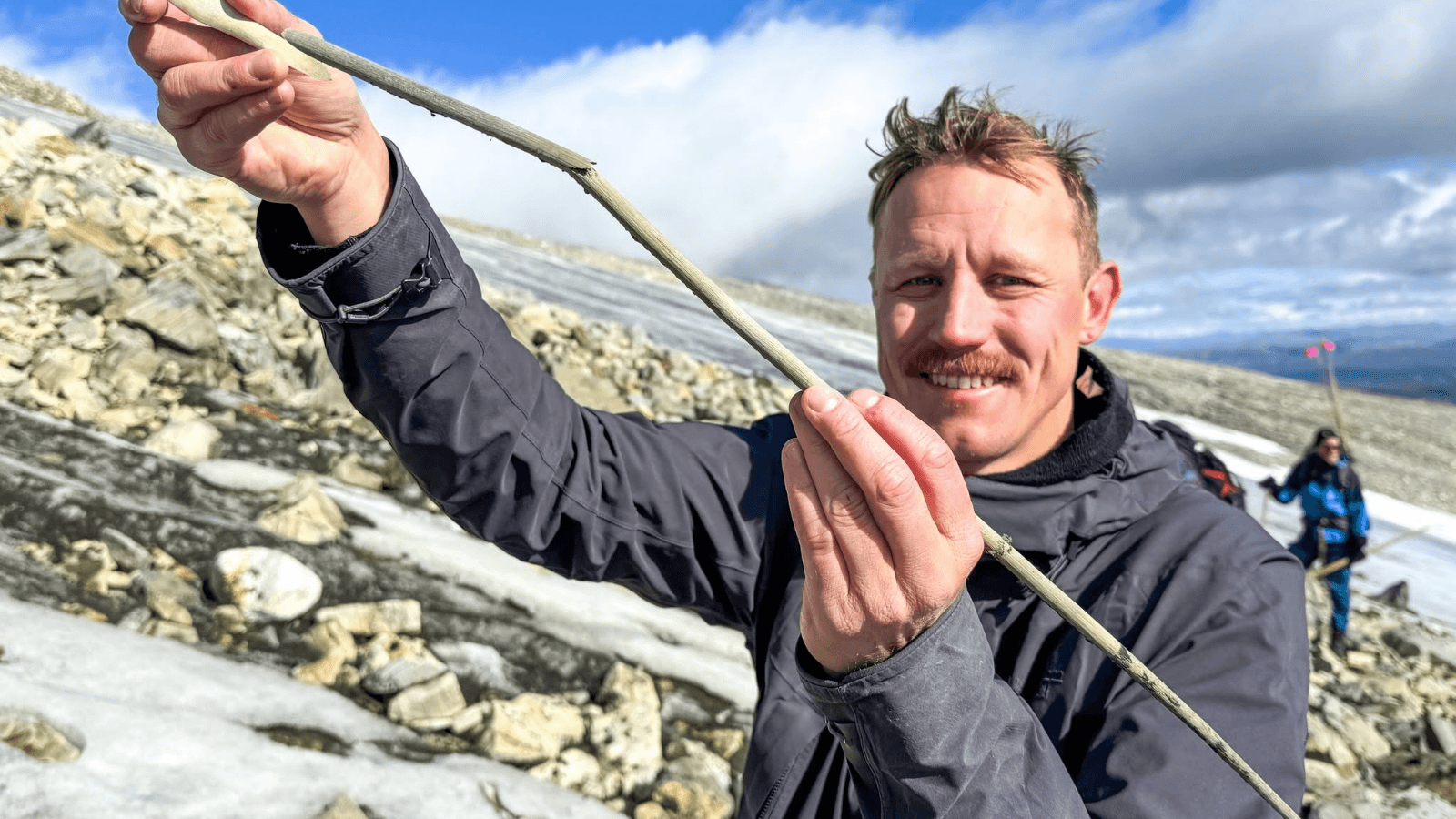 Archaeologist holding a 1,800-year-old bone-tipped arrow recovered from melting ice in Norway.