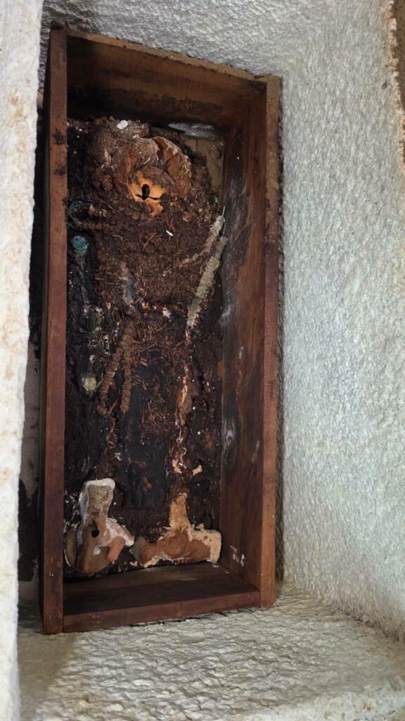 Interior of an ancient Roman child's burial showing skeletal remains, a wooden coffin, and terracotta toys.