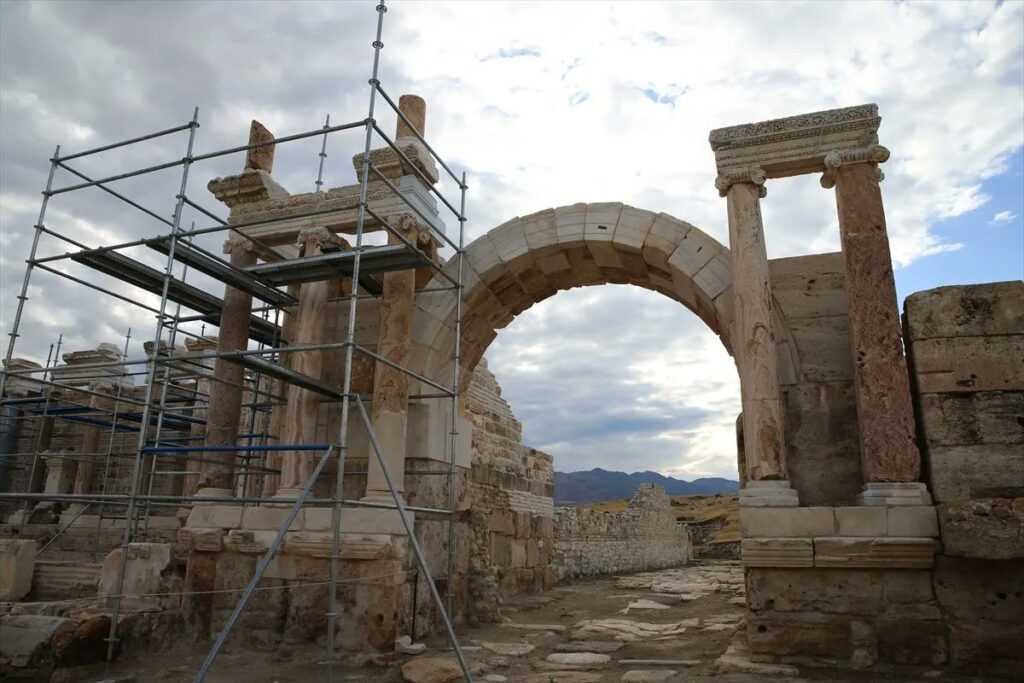 Side view of ancient stone columns, a reconstructed arch and restoration scaffolding at Tripolis.