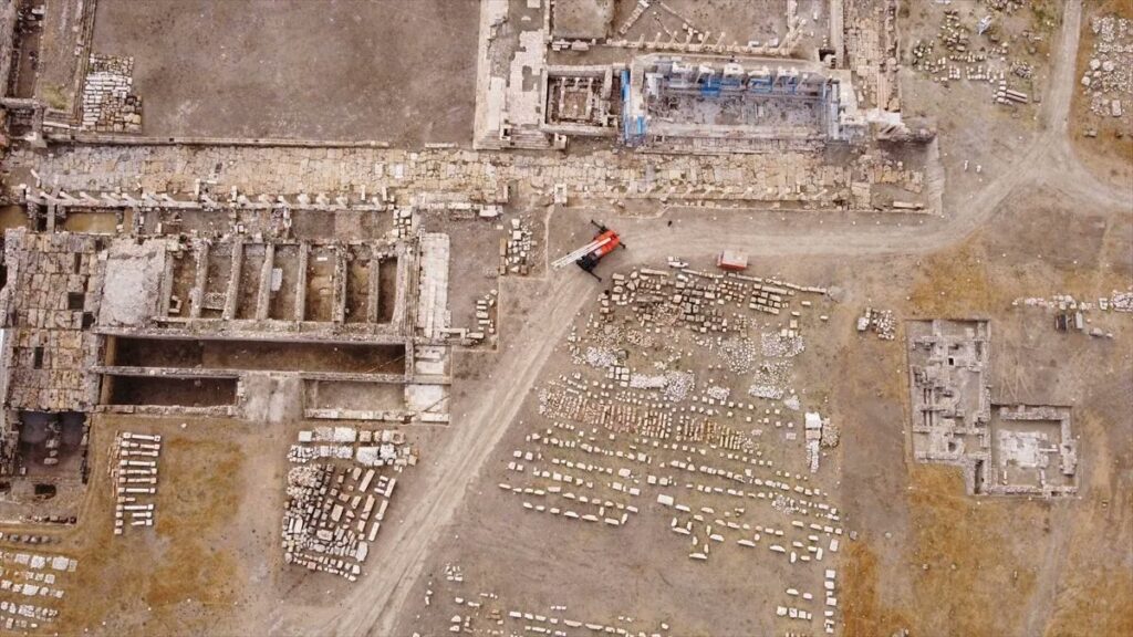 Aerial photograph of the Tripolis archaeological site in Türkiye, with rows of ancient stone blocks and excavated Roman structures.