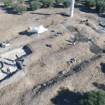 Aerial photograph of archaeologists excavating the Shtyllas temple beside its surviving Doric column.