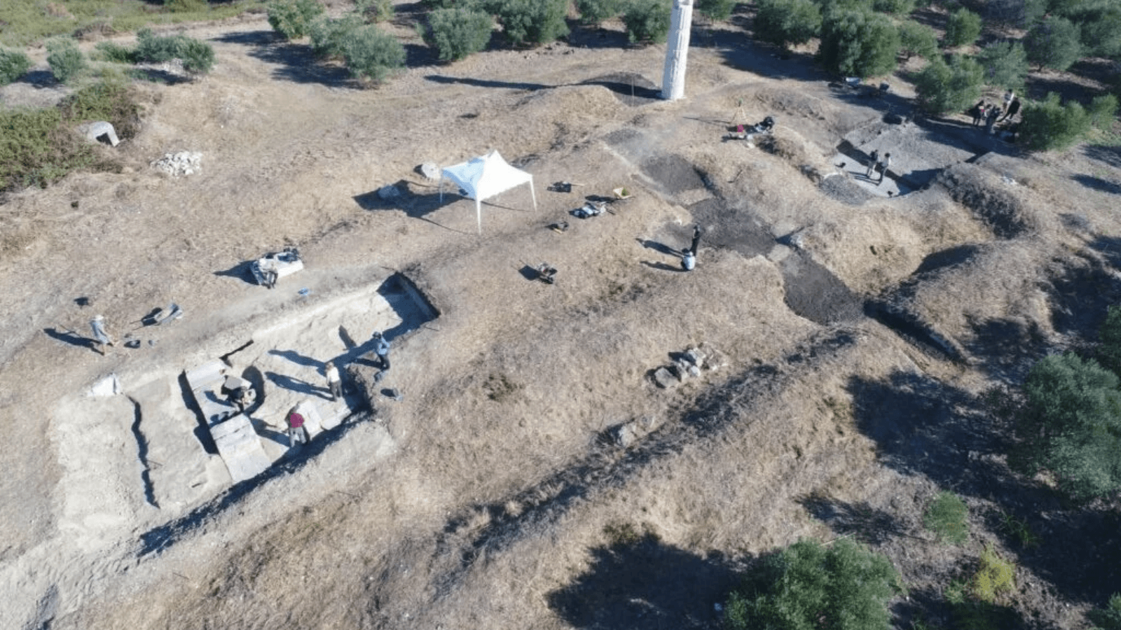 Aerial photograph of archaeologists excavating the Shtyllas temple beside its surviving Doric column.