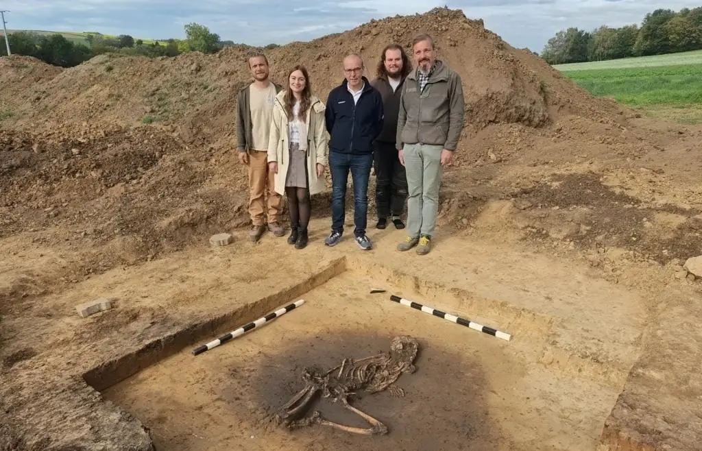 Five people standing beside an excavated Neolithic burial pit containing a 7,000-year-old human skeleton at Großköllnbach in southern Germany.