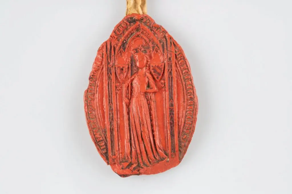 Close-up of the reverse side of a medieval red wax seal. At the center is a heraldic shield with diagonal bands and fleurs-de-lis, enclosed in a decorative quatrefoil frame and surrounded by a circular Latin inscription.