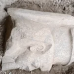 Close-up of the colossal Ramesses II statue head discovered in Egypt, showing the pharaoh's face and crown.
