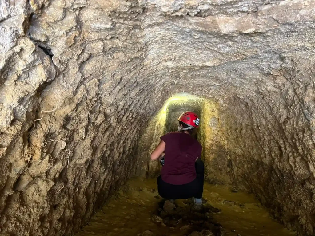 Researcher wearing a red helmet inside an ancient rock-cut underground passage at Case Montana in Agrigento, Sicily.