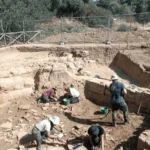 Wide view of archaeologists excavating ancient Greek architectural remains at Case Montana in Sicily.
