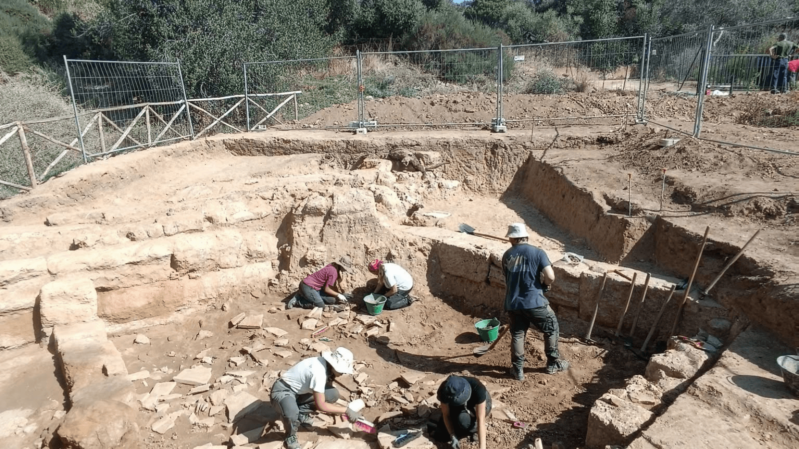 Wide view of archaeologists excavating ancient Greek architectural remains at Case Montana in Sicily.