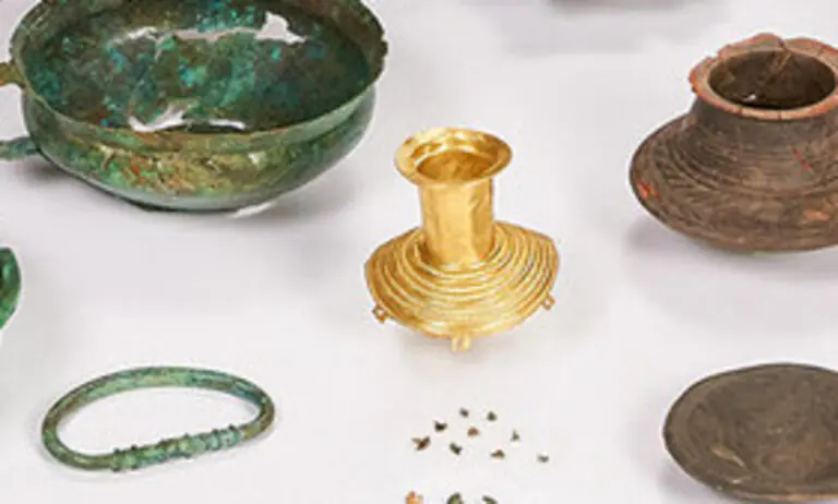 Close-up of a mysterious Bronze Age gold artifact surrounded by pottery and bronze grave goods from Albisheim, Germany.