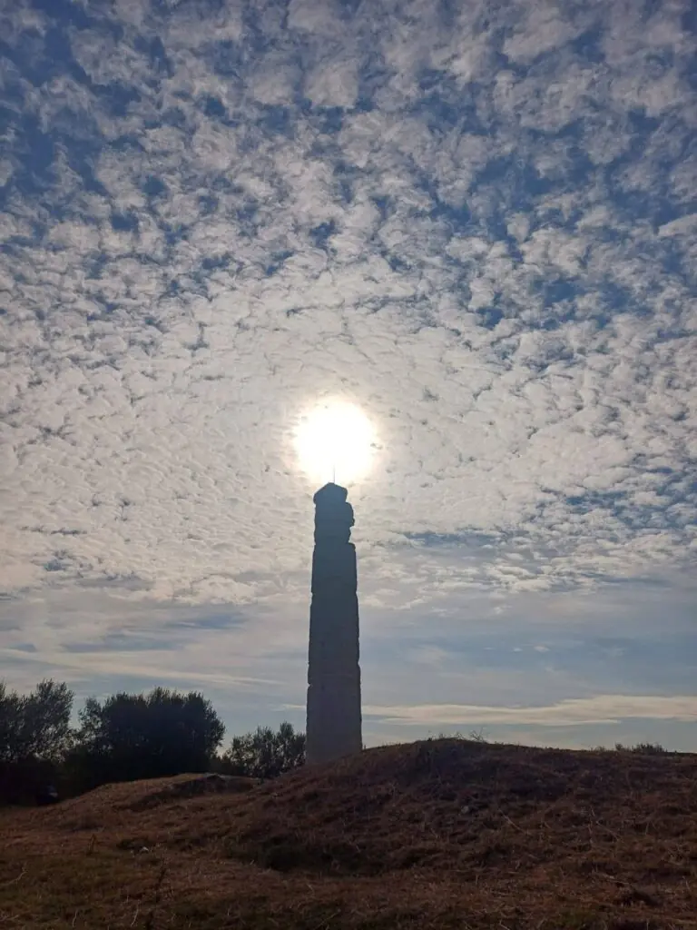 A solitary ancient Doric column rising against a cloudy sky at the Shtyllas archaeological site in Albania.