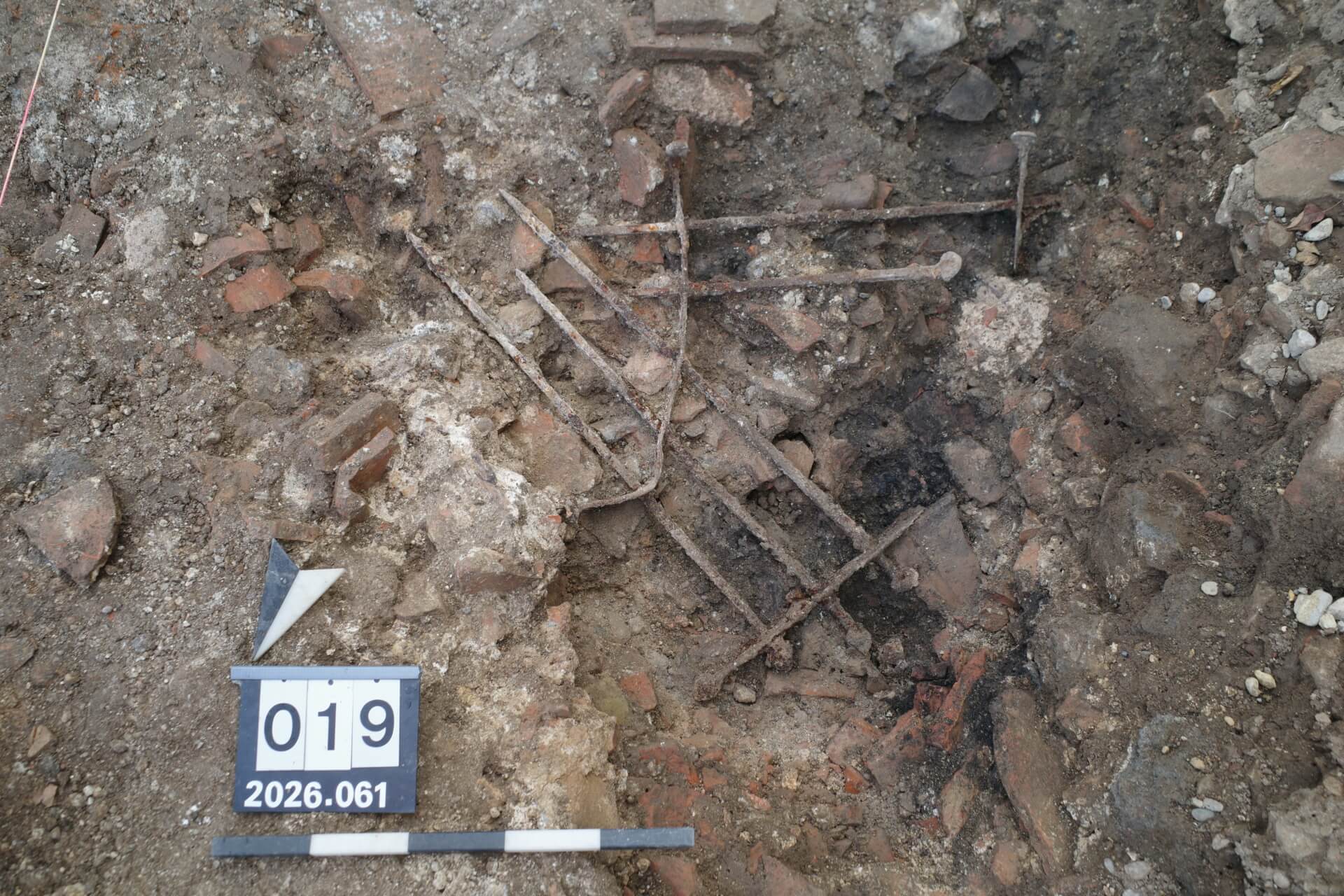 Ancient Roman iron window grille lying among stones and rubble during excavations at Augusta Raurica.