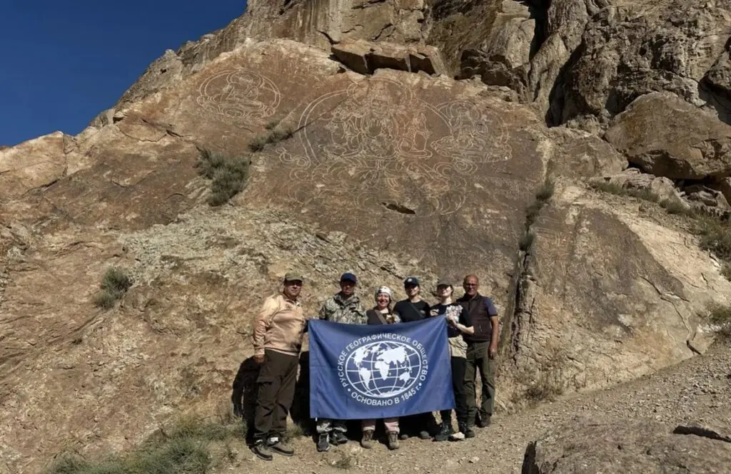 Researchers standing beneath monumental Buddhist rock carvings at Tamgaly-Tas in Kazakhstan.