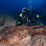 Carabinieri diver examining an ancient Roman amphora on the rocky seabed off Italy's Ligurian coast.