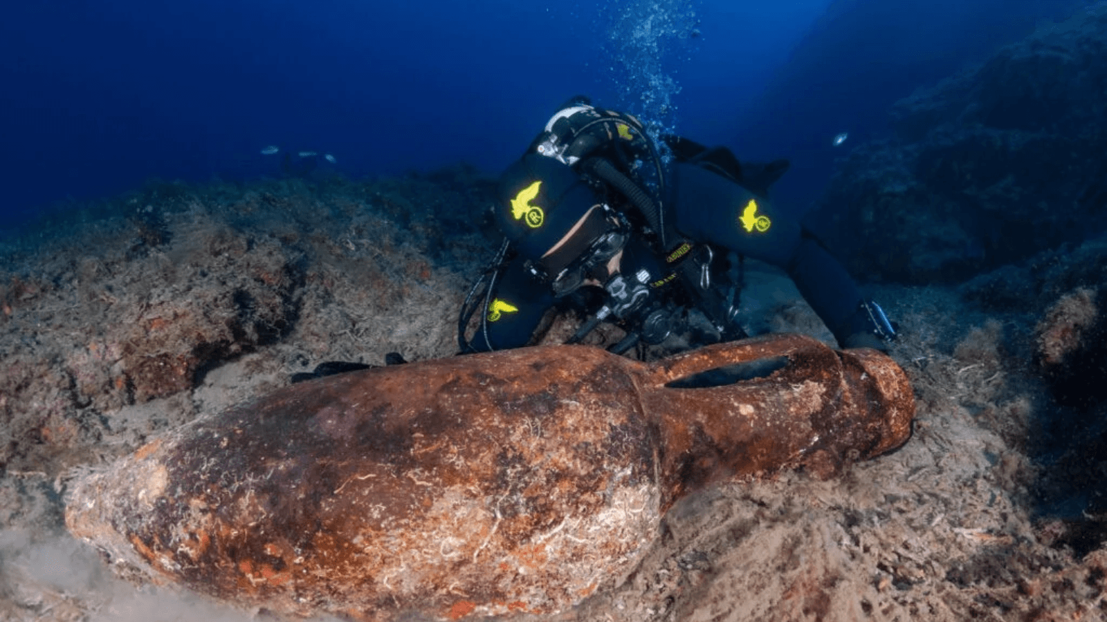 Carabinieri diver examining an ancient Roman amphora on the rocky seabed off Italy's Ligurian coast.