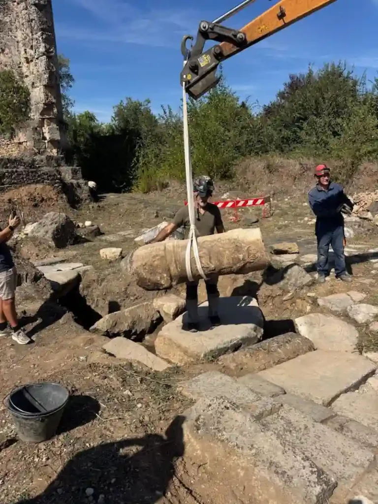 Archaeologists lifting a decorated Roman stone monument from the excavation area at Aquinum.