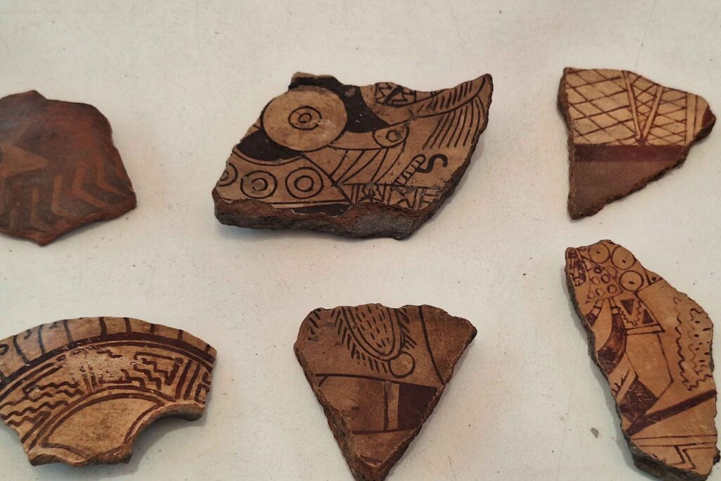 Six ancient pottery fragments decorated with painted geometric patterns and figurative motifs.