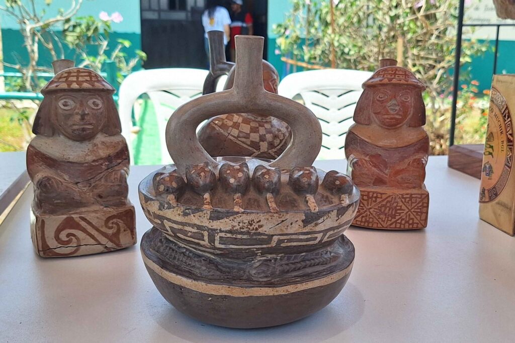 Decorated ceramic vessel with small modeled figures displayed between two seated anthropomorphic pottery sculptures.