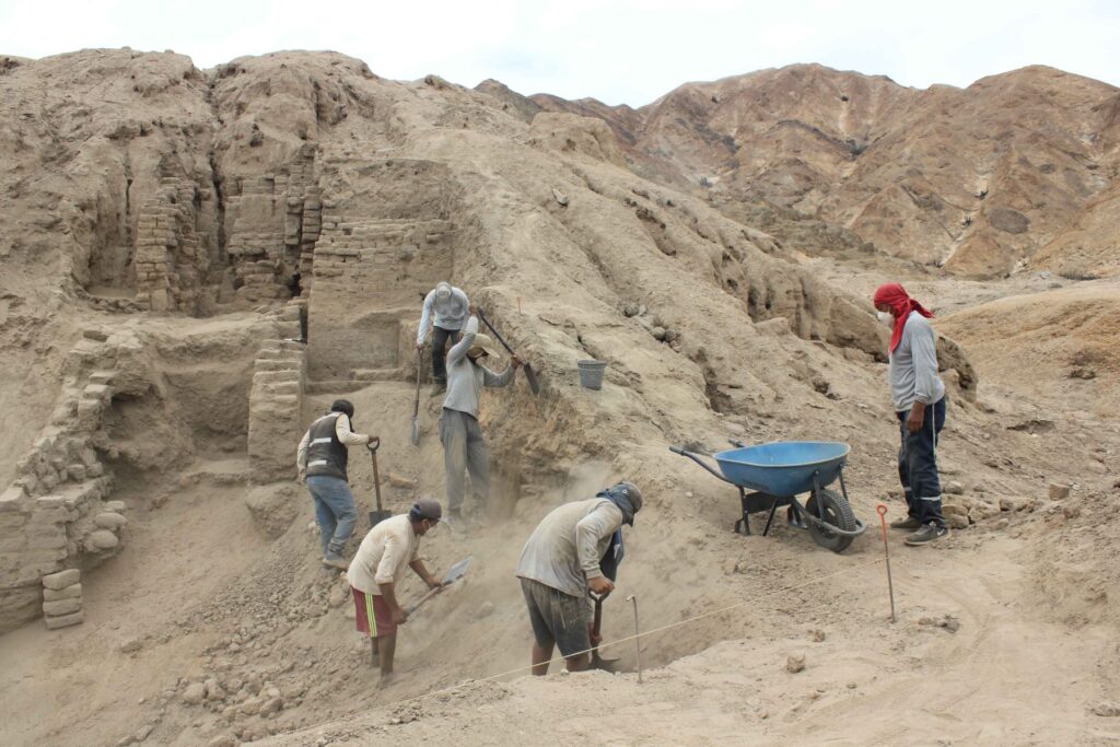Archaeological workers excavating ancient adobe architecture in the desert landscape of northern Peru.
