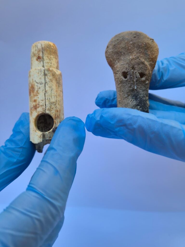 Archaeologists wearing blue gloves hold a bone flute and a 4,500-year-old human-shaped idol head discovered at Troy.