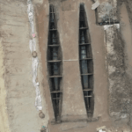 Overhead view of two parallel wooden hulls preserved in a muddy archaeological excavation.